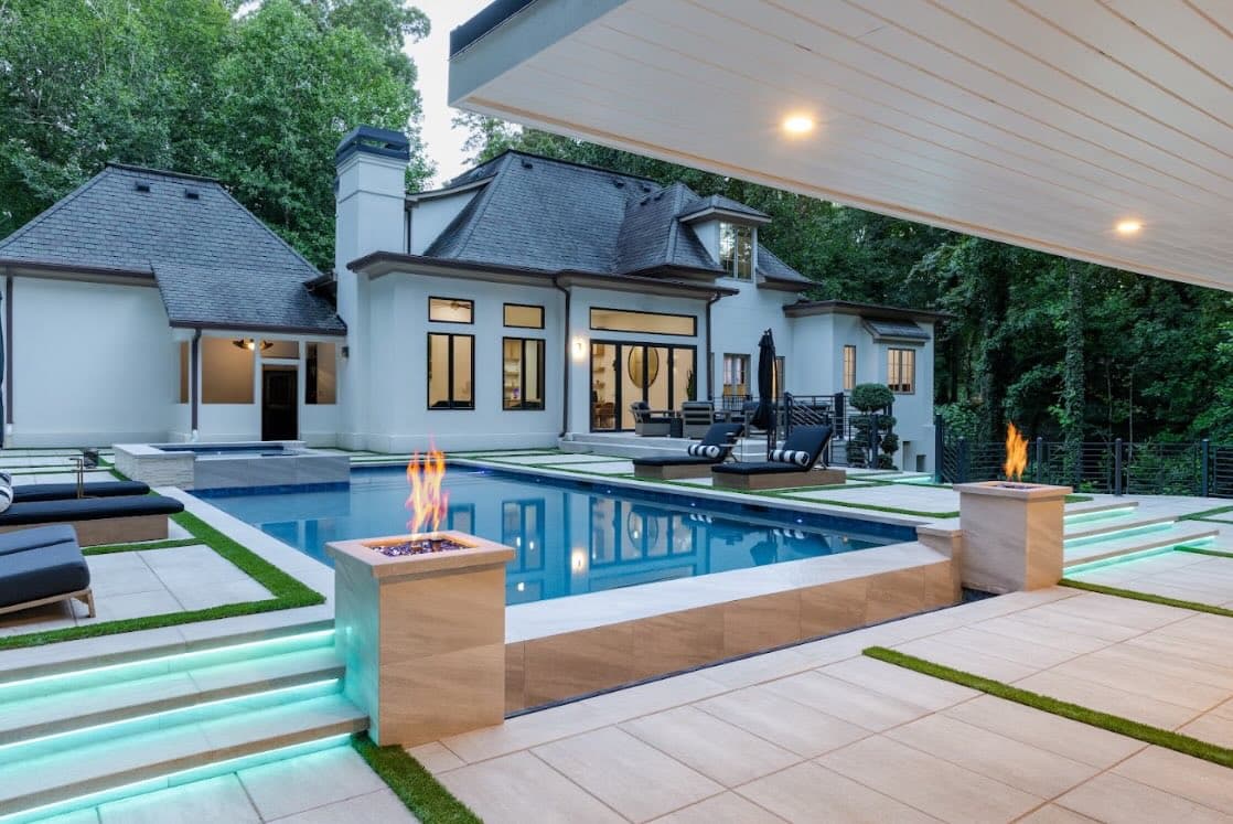 Evening view of the Buckhead pool with fire bowls, illuminated steps, and the home beyond